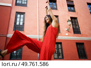 A bright, cheerful young woman joyfully dancing in a vibrant red dress set against a lively and colorful urban backdrop, radiating pure happiness and vitality with every movement she makes. A Joyful Woman is Dancing Outdoors While Wearing a Red Dress in a Beautiful Setting. Стоковое фото, агентство Ingram Publishing / Фотобанк Лори