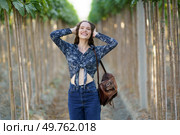 A joyful and spirited young woman poses with her arms raised in a stunning vineyard, exuding true happiness and showcasing her unique style and charm with every single smile she shares. A Joyful Young Woman is Posing Happily in a Lush Vineyard Surrounded by Natures Beauty. Стоковое фото, агентство Ingram Publishing / Фотобанк Лори