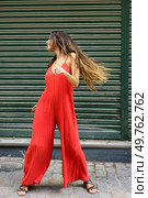 A glamorous young woman exudes confidence as she poses playfully in a trendy red jumpsuit, beautifully showcasing modern fashion against a vibrant green backdrop that complements her stylish look. A Young Woman Stylishly Poses in a Vibrant Red Jumpsuit Against a Lively Green Background. Стоковое фото, агентство Ingram Publishing / Фотобанк Лори