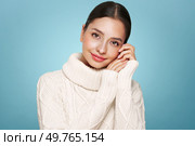 Portrait of young happy beautiful woman smiling and looking away, isolated on blue background in a warm white sweater. Concept of winter promo sale. Стоковое фото, агентство Ingram Publishing / Фотобанк Лори