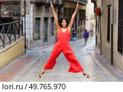 A woman dressed in a bright, vibrant red jumpsuit joyfully leaps and jumps energetically on a picturesque city street, radiating pure happiness, positivity, and exuberant energy for all to see. A Joyful Jump in a Vibrant Red Outfit on a Bustling City Street Full of Energy Today. Стоковое фото, агентство Ingram Publishing / Фотобанк Лори