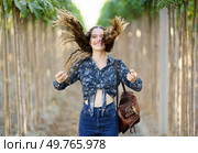 A cheerful young woman stands amidst tall, lush plants, joyfully tossing her hair with a radiant smile, beautifully capturing a moment of pure happiness and delight in nature all around her. A Young Woman Embracing Natures Beauty, with Playful Hair in the Warm Summer Sun. Стоковое фото, агентство Ingram Publishing / Фотобанк Лори