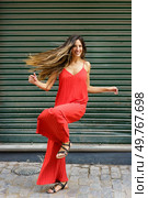 A lively woman dances joyfully in a flowing red dress, her elegant movements and chic style contrasting beautifully against a textured green backdrop, enhancing this delightful scene. A Stylish Woman Gracefully Dancing in a Flowing Red Dress Set Against a Lush Green Background. Стоковое фото, агентство Ingram Publishing / Фотобанк Лори