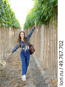 In a colorful vineyard, a carefree young woman strikes a playful pose among green vines and sunlight, embodying adventure and happiness through her cheerful expression and lively setting. A young woman enjoys life walking through a scenic vineyard, taking in natures beauty. Стоковое фото, агентство Ingram Publishing / Фотобанк Лори