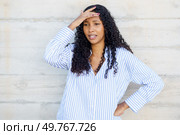 A young woman with curly hair stands pensively against a rough, concrete wall, her expression visibly stressed and deep in thought, as she wears a casual striped shirt that reflects her mood. A stressed young woman holds her head, deep in thought and emotion, facing internal battles. Стоковое фото, агентство Ingram Publishing / Фотобанк Лори