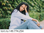 A young woman with flowing, curly hair exudes confidence and charm as she poses gracefully amidst vibrant greenery, embodying the ideals of modern beauty and a cheerful youthful spirit. A Casual Portrait Featuring a Young Woman with Beautiful Curly Hair Surrounded by Nature. Стоковое фото, агентство Ingram Publishing / Фотобанк Лори
