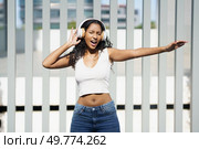 A vibrant and lively young woman dances joyfully to the rhythm of music, wearing her stylish headphones, showcasing her carefree spirit and profound love for music and dance in the open air. An Energetic Young Woman Joyfully Enjoying Her Favorite Music While Wearing Headphones. Стоковое фото, агентство Ingram Publishing / Фотобанк Лори