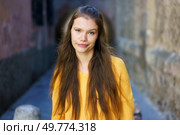 A young woman confidently poses in a cozy alleyway, wearing a vibrant yellow sweater that radiates relaxed, stylish energy, beautifully embodying youthful and contemporary fashion. A Young Woman with a Vibrant Yellow Sweater Poses Happily in a Charming Urban Setting. Стоковое фото, агентство Ingram Publishing / Фотобанк Лори