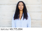 A stylish and fashionable young woman with beautiful, curly hair confidently poses against a rough concrete backdrop while wearing a trendy striped shirt, exuding an aura of elegance and poise. A Confident Young Woman with Beautiful Curly Hair Posing Delightfully Against a Textured Background. Стоковое фото, агентство Ingram Publishing / Фотобанк Лори