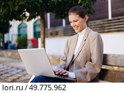 A young woman is happily using her laptop while seated on a bench in a serene outdoor setting, surrounded by lush greenery and the warmth of bright daylight that enhances her joy and focus on work. A Young Woman Happily Working on Her Laptop Outdoors While Sitting on a Bench in the Park. Стоковое фото, агентство Ingram Publishing / Фотобанк Лори