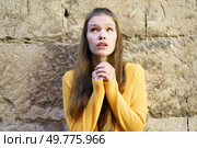 A young woman in a vibrant yellow sweater gazes upward with hope, her emotions beautifully reflected. The rustic stone wall adds depth, creating a striking visual of peace and inspiration. A Young Woman is Expressing Feelings of Hope and Longing Against a Rustic Background Setting. Стоковое фото, агентство Ingram Publishing / Фотобанк Лори