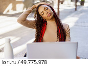 A young woman enjoys a beautiful day outdoors, stretching and working on her laptop, effectively balancing relaxation and productivity, enhancing her wellbeing and sparking creativity. A Young Woman is Enjoying Relaxation While Working on a Laptop in a Modern Outdoor Environment. Стоковое фото, агентство Ingram Publishing / Фотобанк Лори