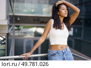 A fashionable young woman with beautiful curly hair poses confidently in a vibrant urban environment, showcasing her modern style, grace, and elegance with an air of selfassuredness and poise. A Stylish Young Woman is Posing Confidently in a Modern and Vibrant Urban Setting. Стоковое фото, агентство Ingram Publishing / Фотобанк Лори