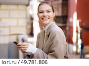 In a bustling city, a confident young woman in a chic outfit smiles while using her smartphone to connect with friends and strangers, showcasing her vibrant social life and modern style. A Smiling Woman in a Stylish Outfit Holding Her Smartphone While Outdoors Enjoying Nature. Стоковое фото, агентство Ingram Publishing / Фотобанк Лори