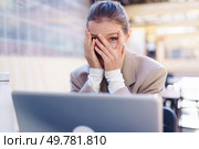 A stressed businesswoman sits at a laptop, covering her face with her hands, showing intense pressure and emotional exhaustion from her professional struggles and productivity demands. A stressed businesswoman is covering her face in front of her laptop while working. Стоковое фото, агентство Ingram Publishing / Фотобанк Лори
