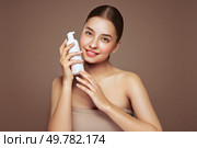 A young woman shows off a bottle with a foam dispenser for washing. Daily skin care cosmetics advertisement. Studio shoot Beige background. Стоковое фото, агентство Ingram Publishing / Фотобанк Лори