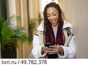 A vibrant woman with beautifully braided hair smiles joyfully at her smartphone, a moment captured perfectly in a stylish urban setting that radiates modernity, color, and irresistible charm. A Joyful Woman Engaged with Her Smartphone While Enjoying an Urban Setting Around Her. Стоковое фото, агентство Ingram Publishing / Фотобанк Лори