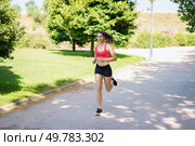 A young woman experiences happiness while jogging in a scenic park, demonstrating fitness, health, and an active lifestyle intertwined with nature to symbolize resilience and vigor. A young woman is jogging in the park, enjoying nature, exercising, and embracing a healthy lifestyle. Стоковое фото, агентство Ingram Publishing / Фотобанк Лори
