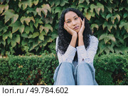 A young woman sits pensively amidst the vibrant and lush green foliage, showcasing her casual yet fashionable style while lost in thought, reflecting her contemplative mood and emotions. This is a thoughtful young woman dressed in casual attire, surrounded by lush greenery. Стоковое фото, агентство Ingram Publishing / Фотобанк Лори