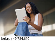 A cheerful young woman happily enjoys using her tablet in a relaxed outdoor environment, showcasing the blend of modern technology with a vibrant lifestyle amid the beauty of nature. A young woman is engaging with her tablet in a relaxed and casual outdoor setting. Стоковое фото, агентство Ingram Publishing / Фотобанк Лори
