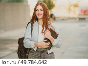A cheerful and lively young woman with beautiful wavy red hair is happily holding several books while she walks confidently along an urban street, showcasing a vibrant and active student lifestyle. A smiling young woman joyfully carrying books while casually walking along an urban street. Стоковое фото, агентство Ingram Publishing / Фотобанк Лори