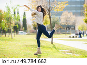 A cheerful young woman dances joyfully and energetically in a beautiful sunlit park, surrounded by vibrant autumn colors and lush greenery, creating a lively atmosphere of happiness and fun. A Joyful Young Woman Dancing and Having Fun Outdoors in a Beautiful Autumn Park Scene. Стоковое фото, агентство Ingram Publishing / Фотобанк Лори