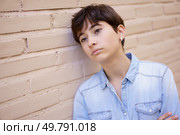 A young individual with stylishly cut short hair is leaning thoughtfully against an appealing beige brick wall, lost in contemplation and reflecting on a myriad of deep emotions within. A Young Person Engaged in Contemplation as They Lean Against a Wall, Deep in Thought. Стоковое фото, агентство Ingram Publishing / Фотобанк Лори
