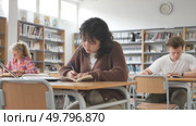 Focused asian teenager female student sitting at library desk, preparing for exam. Стоковое видео, видеограф Яков Филимонов / Фотобанк Лори