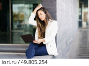 A fashionable woman sits on city steps, focused on her tablet, blending work with the vibrant urban energy, showcasing the dynamic intersection of technology and modern professional life. A woman in a stylish white blazer is engaged with her tablet in a modern urban setting. Стоковое фото, агентство Ingram Publishing / Фотобанк Лори