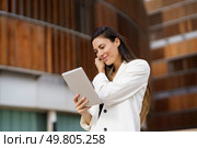 A confident woman in a stylish white blazer interacts with her tablet, showcasing modern technology in an elegant environment. A Professional Woman Engaged with a Tablet in a Modern and Stylish Setting Outdoors. Стоковое фото, агентство Ingram Publishing / Фотобанк Лори