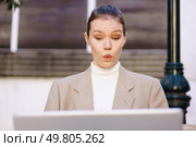 A businesswoman expresses astonishment while diligently working on her laptop outdoors, blending professionalism with surprise, highlighting remote work and urban creativity where innovation thrives. A Surprised Businesswoman is Working Deliberately on Her Laptop While in an Outdoor Setting. Стоковое фото, агентство Ingram Publishing / Фотобанк Лори