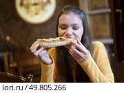 In a cozy restaurant, a young woman enjoys a delicious pizza topped with fresh ingredients, relishing every bite in a warm atmosphere filled with laughter and the aroma of tasty food. Delicious Pizza Enjoyment A Young Woman Fully Relishing Her Meal and Assets of Happiness. Стоковое фото, агентство Ingram Publishing / Фотобанк Лори