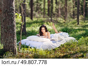 Young woman is reading a book in the forest lying on a mattress. The girl relaxing in nature. Стоковое фото, агентство Ingram Publishing / Фотобанк Лори