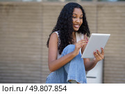 A cheerful and lively young woman is happily interacting with her tablet, effectively showcasing the significant role that technology plays in our daily lives, especially in an outdoor setting. A young woman is engaged with her tablet while sitting outdoors in a vibrant urban setting. Стоковое фото, агентство Ingram Publishing / Фотобанк Лори
