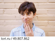 A young individual with stylish short hair, clearly deep in thought, gently rests their hand on their chin, conveying a sense of contemplation while positioned in front of a textured old brick wall. A thoughtful young individual stands against a rustic brick wall, lost in deep contemplation. Стоковое фото, агентство Ingram Publishing / Фотобанк Лори