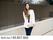 A stylish and confident businesswoman poses outdoors, dressed in a chic white blazer paired with trendy jeans, effectively showcasing a modern, professional look that embodies sophistication. A fashionable and stylish businesswoman is confidently posing outdoors in her chic white blazer. Стоковое фото, агентство Ingram Publishing / Фотобанк Лори
