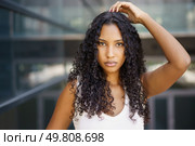 A confident young woman with styled curly hair poses outdoors, highlighting her features and radiant expression against a modern backdrop that enhances her natural elegance and charm. A Confident Young Woman Showcasing Her Curly Hair While Posing Outdoors in Style. Стоковое фото, агентство Ingram Publishing / Фотобанк Лори