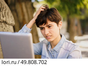 In a calming outdoor setting, a young individual sits alone, frustrated and overwhelmed, working intently on their laptop, showing deep confusion and stress despite the peaceful surroundings. A frustrated young individual is struggling with their laptop while outdoors in a serene setting, Стоковое фото, агентство Ingram Publishing / Фотобанк Лори