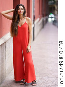 In a charming urban setting, a stylish woman stands confidently in a striking red jumpsuit, effortlessly showcasing a relaxed yet chic vibe that perfectly blends comfort with elegance and fashion. A Fashionable Woman Dressed in a Vibrant Red Jumpsuit Strolling Along an Urban Street. Стоковое фото, агентство Ingram Publishing / Фотобанк Лори