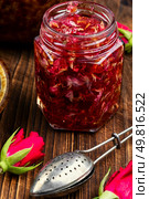 Jar with rose jam and flower on wooden surface, rose petals jam and tea cooking utensils.. Rose jam in a glass jar. Стоковое фото, агентство Ingram Publishing / Фотобанк Лори