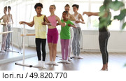 Multiethnic group of teenage girls and boys, ballet class students, practicing demi plie at barre during lesson for beginners under guidance of female teacher in light-filled choreography studio. Стоковое видео, видеограф Яков Филимонов / Фотобанк Лори