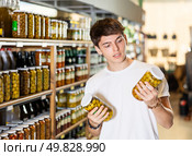 Young guy in supermarket selects examines compares two cans of olives. Стоковое фото, фотограф Яков Филимонов / Фотобанк Лори
