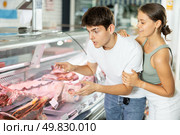 Young man and woman purchasers buying meat in butcher shop. Стоковое фото, фотограф Яков Филимонов / Фотобанк Лори