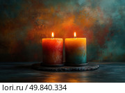 Two massive scented candles burning with a warm, even flame. The candles are placed next to each other on a dark round stand and create an atmosphere of coziness and tranquility. Their surface is painted with smooth gradients in deep shades of red, yellow, orange and turquoise, creating an artistic effect. The background is made in a rich textured painting with transitions from dark blue to orange-red, emphasizing the warmth of the light and creating a meditative mood. Ideal for themes: coziness, relaxation, aromatherapy, interior, romance, handmade candles. Стоковое AI-изображение, AI-художник Анна Кривицкая / Фотобанк Лори