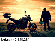 Biker standing with its motorbike on a misty sunset. Стоковое фото, агентство Ingram Publishing / Фотобанк Лори