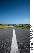 Expansive Rural Road Leading Towards Distant Rolling Hills Under a Clear Blue Sky. Стоковое AI-изображение, AI-художник Юлия Гапеенко / Фотобанк Лори