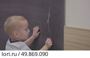 A young child is enthusiastically drawing on a chalkboard in a lively classroom setting. Стоковое видео, видеограф Olesia Kondrateva / Фотобанк Лори