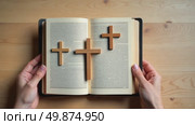 Three wooden crosses on an open Holy Bible held by hands. Concept of Christian faith, Easter, and the crucifixion of Jesus Christ. Top view. Стоковое AI-видео, аниматор Sergey Grishin / Фотобанк Лори