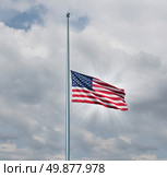 Half mast American flag concept with the symbol of the United States flying at low level on the flagpole or staff on a cloudy day with a sun glow as an icon of honor respect and mourning for fallen heros. Стоковое фото, агентство Ingram Publishing / Фотобанк Лори
