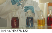 A laboratory technician in a white coat and protective gloves pours liquid into a chemical dish. Стоковое видео, видеограф Aleksey Kidisyuk / Фотобанк Лори